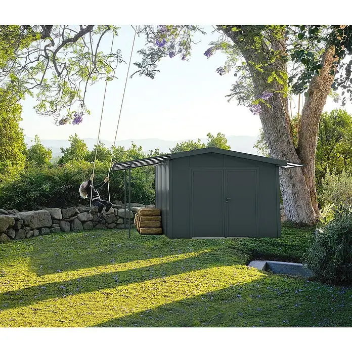 Wismar-NFI Gerätehaus Marguerite 33 - Außenmaß inkl. Dachüberstand (B x T): 505 x 385 cm, Stahl, Anthrazit/Weiß - Bild einer grauen Gerätehütte im Garten mit einem Schaukelgerüst und einer Person, die schaukelt.