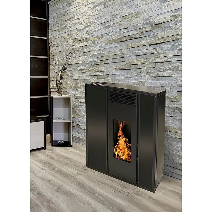 Pelletofen Tessa - 8,8 kW, Raumheizvermögen: 300 m³, 0,94 kg/h - 1,98 kg/h, Farbe Verkleidung: Schwarz - Kaminofen mit Steinwand im Hintergrund. Das Feuer brennt hell im Ofen und sorgt für eine gemütliche Atmosphäre im Raum. Elegantes Design.