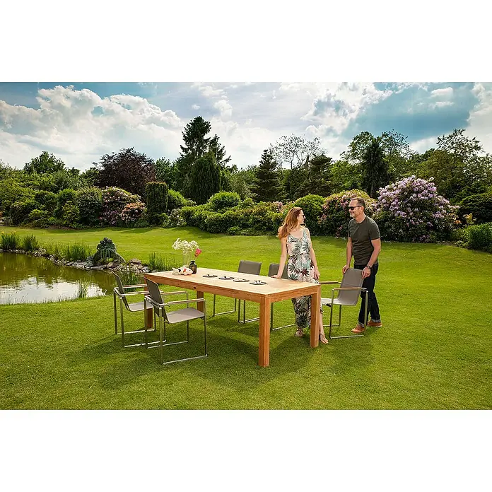 Kai Wiechmann Gartentisch - L x B x H: 180 x 90 x 76 cm, Teakholz, Rechteckig, Naturbelassen - Ein geräumiger Gartentisch aus Holz mit passenden Stühlen steht im Garten. Ein Paar genießt die Aussicht.