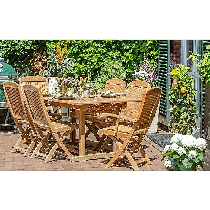 Kai Wiechmann Gartentisch - L x B x H: 240 x 120 x 75 cm, Teak, Rechteckig, Naturbelassen - Eine Gartenszene mit einem Teakholztisch und Stühlen, gedeckt mit Geschirr und Gläsern, umgeben von üppigem Grün und Blumen.