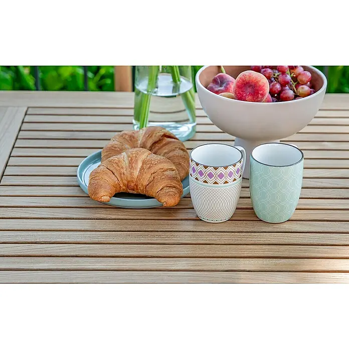 Kai Wiechmann Gartentisch - L x B x H: 100 x 70 x 75 cm, Teakholz, Rechteckig, Naturbelassen - Ein Arrangement aus zwei verzierten Tassen, Croissants, Obst und einer Vase auf einem hellen Holztisch im Freien.