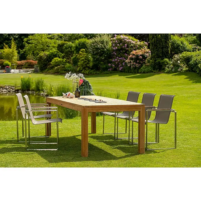 Kai Wiechmann Gartentisch - L x B x H: 150 x 90 x 76 cm, Teakholz, Rechteckig, Naturbelassen - Ein Gartentisch-Set mit einem Holztisch und modernen Stühlen auf einem grünen Rasen in einer malerischen Gartenumgebung.