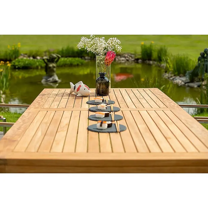 Kai Wiechmann Gartentisch - L x B x H: 150 x 90 x 76 cm, Teakholz, Rechteckig, Naturbelassen - Eine Nahaufnahme eines Holztisches mit Sushi-Tellern, Blumen und einer Fischfigur vor einem ruhigen Teich.