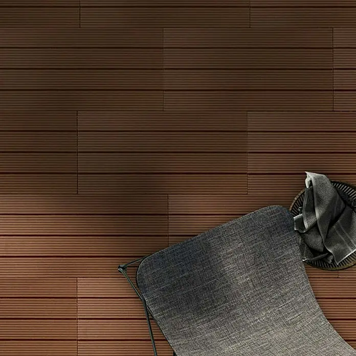 Floordirekt Klickfliese WPC Royal 30 x 60 cm Hellbraun - 60 x 30 x 2,2 cm, 1 Stk. - Nahaufnahme einer braunen Terrassendiele mit einer grauen Gartenliege und einem Handtuchkorb. Das Bild zeigt das Terrassendielenmuster.