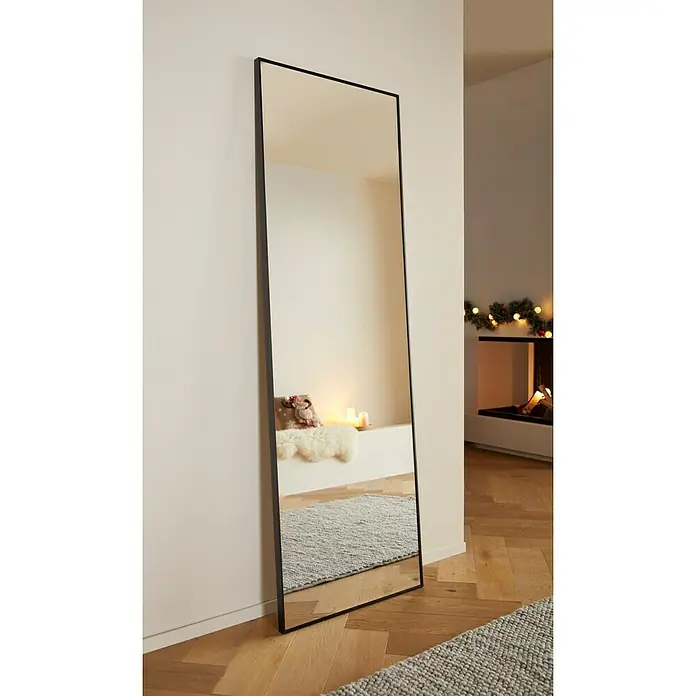 Rahmenspiegel Levi - 60 x 180 cm, Schwarz, Aluminium - Ein schmaler, rechteckiger Spiegel mit einem schwarzen Rahmen lehnt an einer weißen Wand und spiegelt ein Zimmer mit dekorativen Elementen wider.