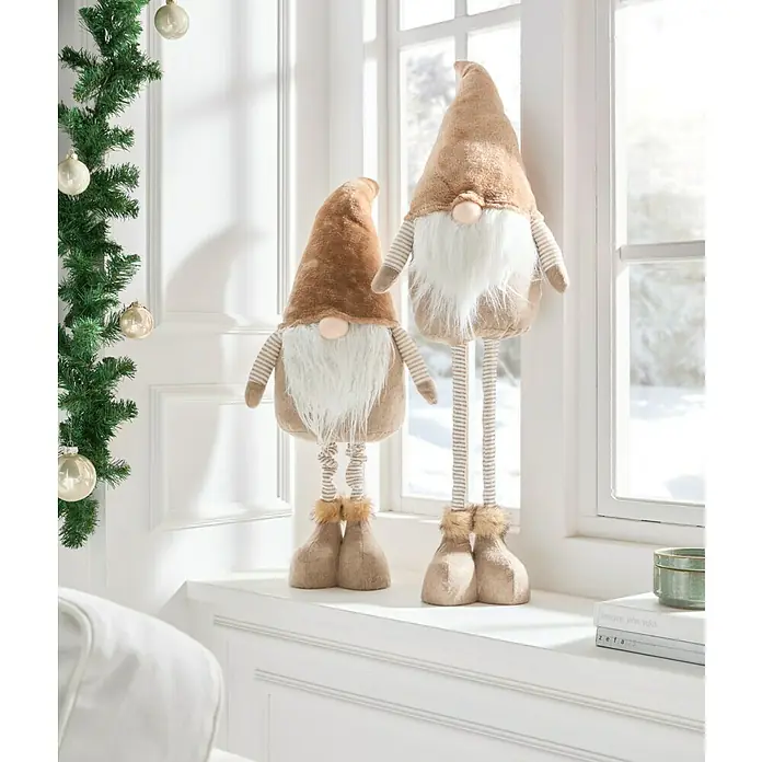 Dekofigur Wichtel - Braun/ Beige, Textil - Zwei festliche Zwerge aus Stoff mit gestreiften Beinen, Fellakzenten und Weihnachtsmütze sitzen auf einem Fensterbrett neben einem Tannenzweig.