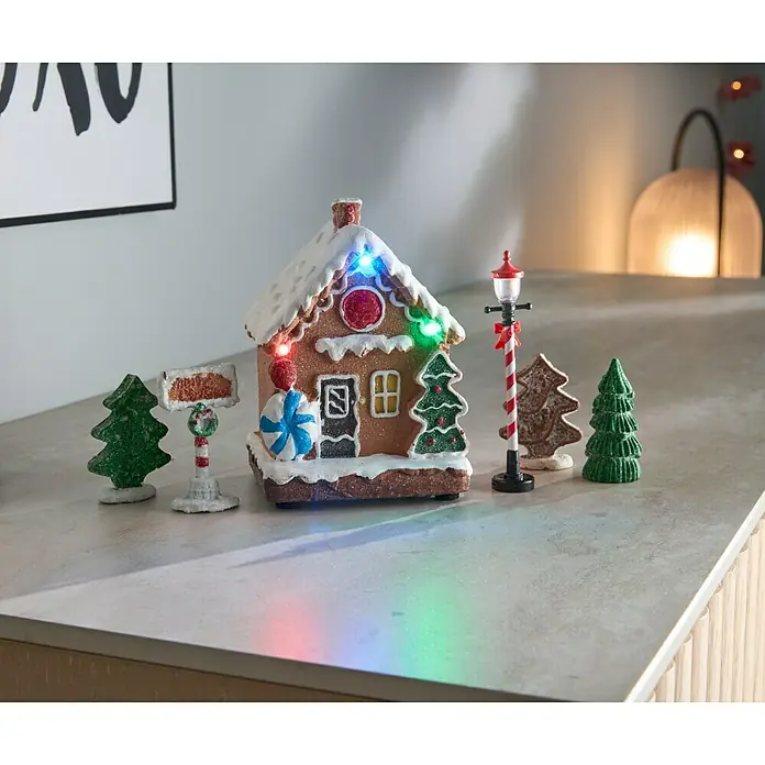 LED-Weihnachtsdorf Lebkuchenhaus - 9,5 x 9,5 x 13 cm, LED, Batteriebetrieben - Eine festliche Lebkuchenhaus-Szene mit funkelnden Lichtern, kleinen Weihnachtsbäumen und einer dekorativen Straßenlaterne, ideal für die Feiertagsdekoration.