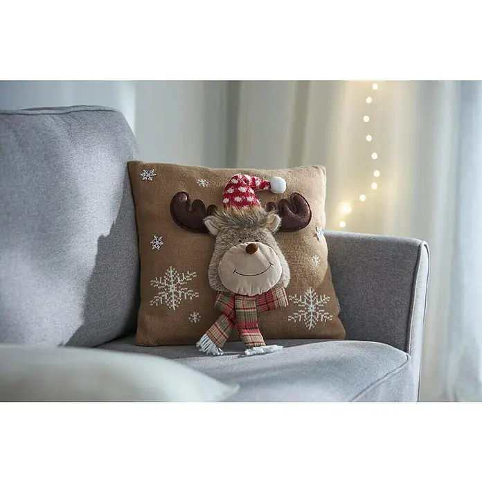 Kissen Rentier - Beige, L x H: 40 x 40 cm - Weihnachtliche Dekoration: Ein Kissen mit einem Rentier mit roter Mütze und Schal auf einem grauen Sessel.