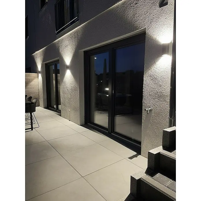 Ledvance Aplique exterior LED - 12 W, 5,5 cm x 9 mm x 16 cm, Gris oscuro, Claro, IP44 - Foto exterior de una casa moderna con iluminación de patio y grandes ventanales correderas que iluminan la zona exterior.