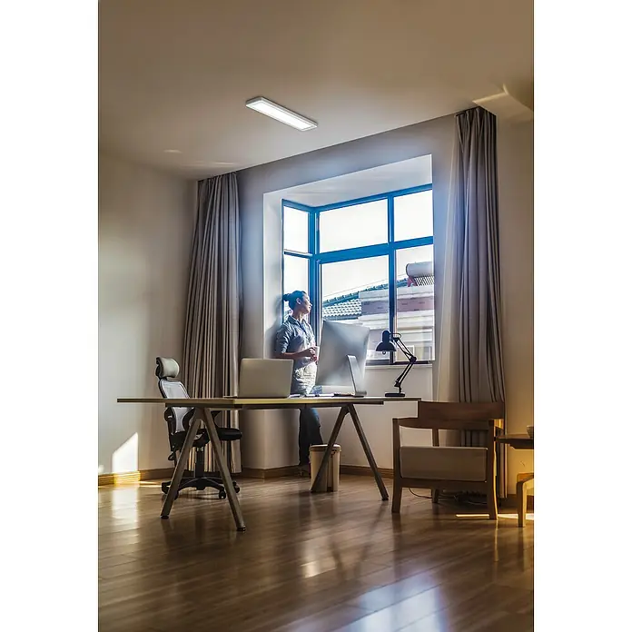Ledvance LED-Deckenleuchte Office Line - 25 W, L x B x H: 61,5 x 13 x 2,5 cm, Weiß, Neutralweiß - Helles, rechteckiges LED-Panel an der Decke eines Büros mit Schreibtisch, Stuhl und einer Person am Fenster für angenehme Beleuchtung.