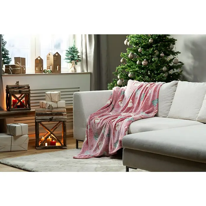 Decke Cherry Xmas - Glow in the Dark - Rot, 180 x 140 cm, 100 % Polyester - Nahaufnahme einer weichen, rosa Weihnachtsfleece-Decke auf einem Sofa mit festlicher Dekoration im Hintergrund.