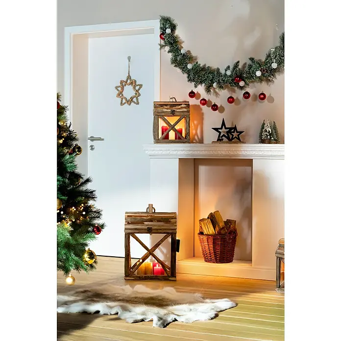 Edelmann Weihnachtsgirlande Kaprun - Kunststoff, LED-Beleuchtung - Weihnachtliche Szene mit Baum, Kamin und rustikalen Holzlaternen, die warmes Kerzenlicht verbreiten und eine festliche Atmosphäre schaffen.