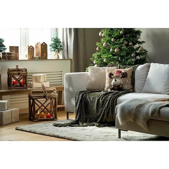 Kissen Rentier - Beige, L x H: 40 x 40 cm - Festliche Szene mit Weihnachtsbaum, Sofa mit Kissen und Decken sowie Holzlaternen mit Kerzen, die eine gemütliche Weihnachtsstimmung verbreiten.