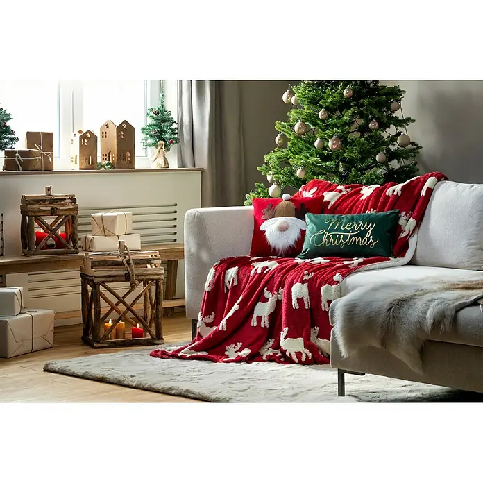 Kissen Santa - Rot, L x H: 40 x 40 cm - Festliches Wohnzimmer mit Weihnachtsdeko. Im Fokus: Eine rote Decke mit Rentier-Muster auf dem Sofa, umgeben von weihnachtlichen Elementen.