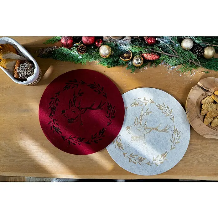Tisch-Set Hirsch - 1 Stk., Sortiert, Durchmesser: 38 cm - Festlicher Tisch mit roten und weißen Filzplatzsets, verziert mit einem Hirschmotiv, umrahmt von einem dekorativen Blätterkranz für eine weihnachtliche Atmosphäre.