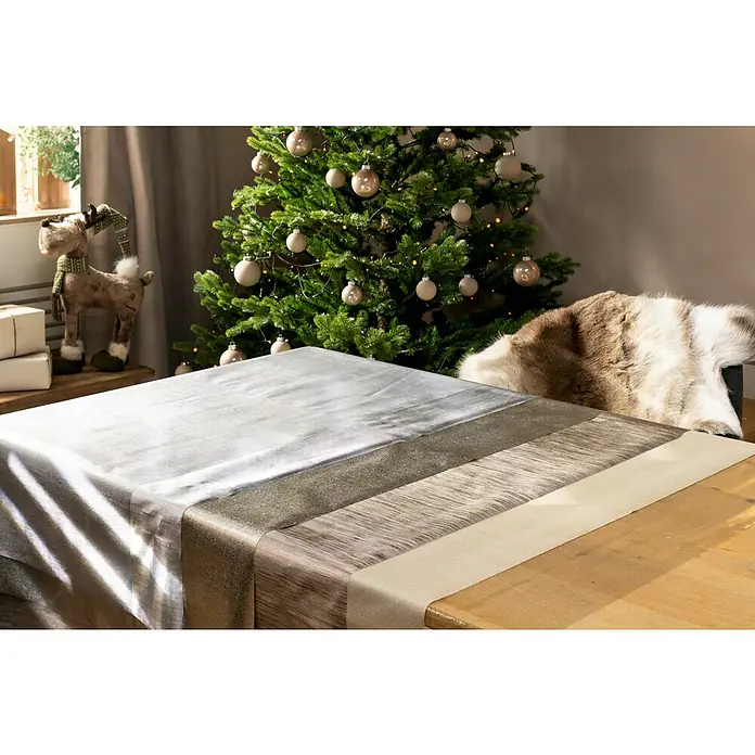 Tischdecke - Metall Optik Fiber Cuvee, 220 x 140 cm, Rechteckig - Festlicher Tisch mit einer eleganten Tischdecke, die in verschiedenen metallischen Farben schimmert, neben einem geschmückten Weihnachtsbaum.