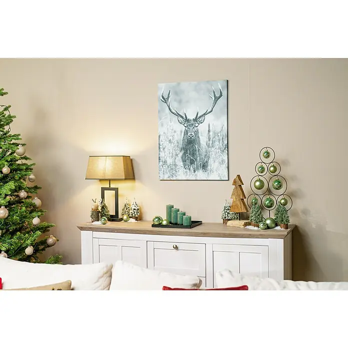 Stumpenkerzen-Set Rustic Safe - 4 -tlg., Smaragd - Festliche Dekoration: Ein Hirsch-Wandbild, grüne Kerzen und ein Baumschmuck auf einem Sideboard, umgeben von Weihnachtsbaum und Sofakissen.