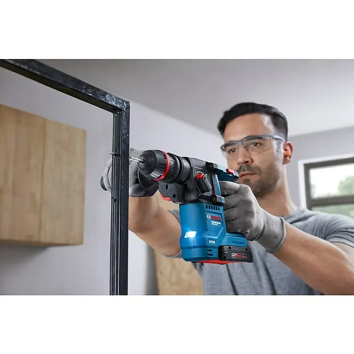 Bosch Professional AMPShare 18V Akku-Bohrhammer GBH 18V-18X - 18 V, Ohne Akku, 1,5 J - Ein Mann bohrt mit einem blauen Bosch-Bohrhammer ein Loch in einen Metallrahmen. Er trägt Schutzbrille und Handschuhe.