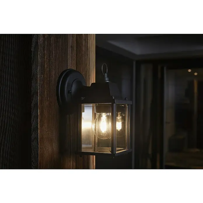 Osram LED-Wandleuchte Endura Classic Laterne - Schwarz - Nahaufnahme einer stilvollen schwarzen Außenwandleuchte mit einer warm leuchtenden Glühbirne an einer rustikalen Holzwand.