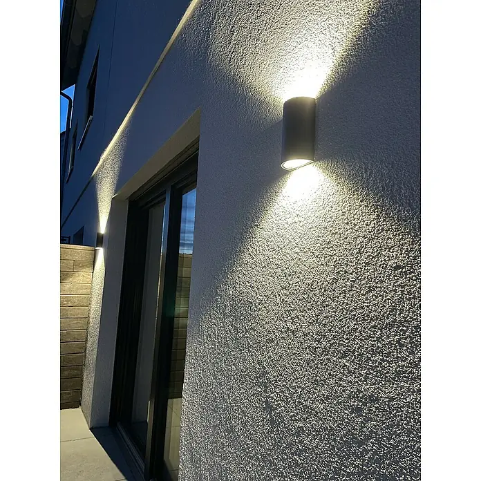 Ledvance Aplique exterior LED - 12 W, 5,5 cm x 9 mm x 16 cm, Gris oscuro, Claro, IP44 - Lámpara de pared en forma de cilindro en una pared exterior texturizada, que emite una luz cálida hacia arriba y abajo.