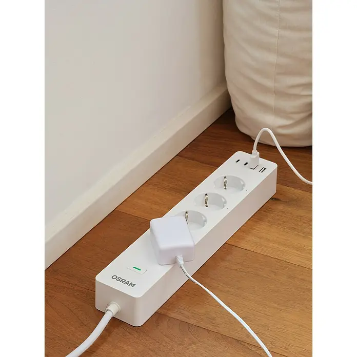 Osram Smart+ Smart-Steckdosenleiste 2. Gen. 2 USB-A, 2 USB-C - Weiß - Steckdosenleiste von Osram mit eingesteckten Geräten auf einem Holzboden, bietet zusätzliche Steckplätze und USB-Anschlüsse für einfache Stromversorgung.