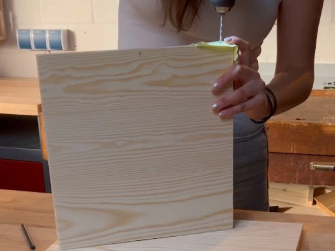 Ein Loch wird mit dem Akkubohrer in die Seite einer Holzplatte gebohrt
