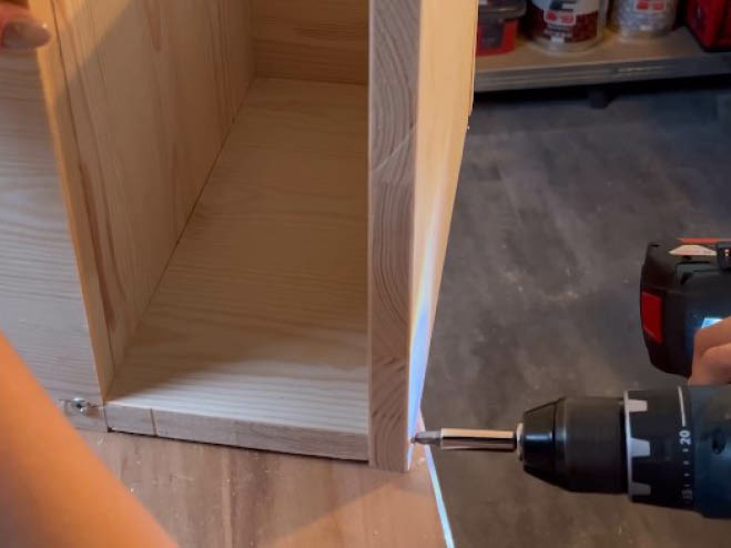 Eine Holzplatte wird zum Gestell vom Beistelltisch angeschraubt