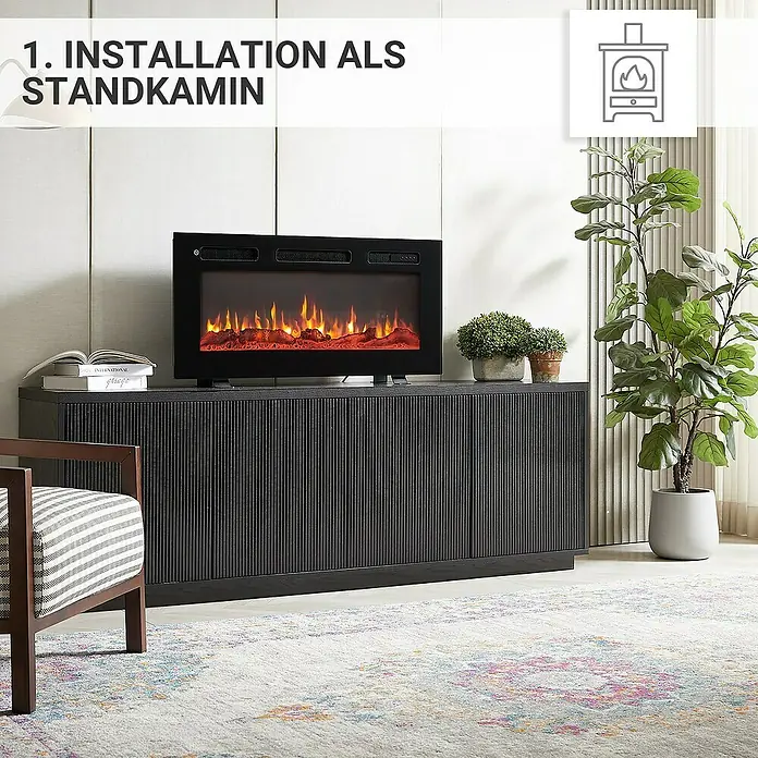 Balderia Elektrischer Kamin LE-36 3D-Flammeneffekt - Schwarz, 92 x 14 x 43 cm - Installation eines elektrischen Kamins als Standkamin auf einem schwarzen Sideboard, daneben eine Zimmerpflanze und ein Stuhl.