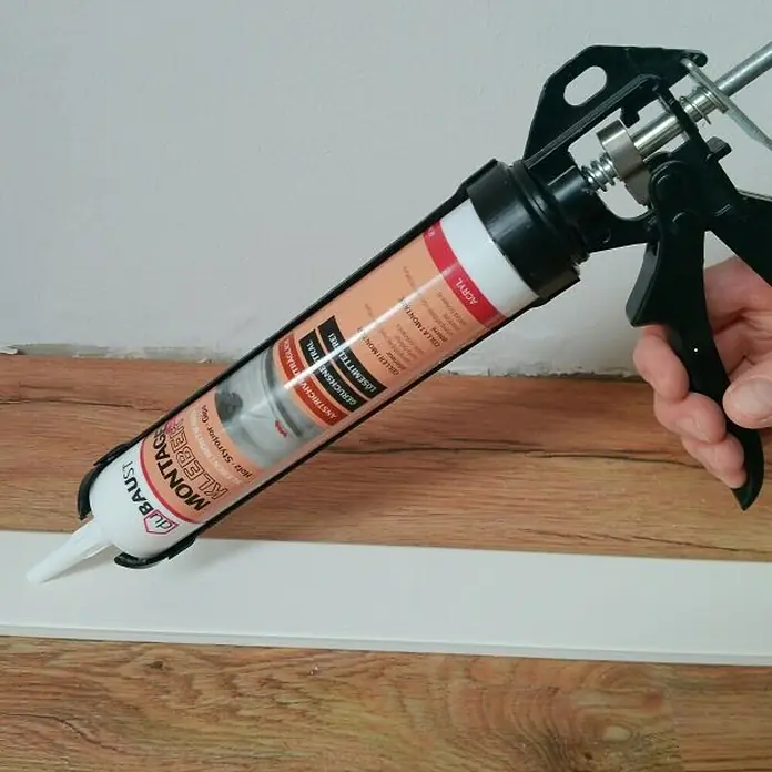 DuBaust Montagekleber Montagekleber - 504 g, Kartusche - Eine Kartuschenpistole wird verwendet, um Montagekleber auf eine weiße Leiste aufzutragen, ideal für Holz- und Styroporarbeiten.