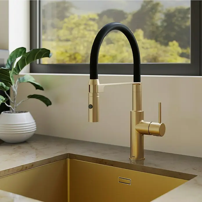 Lenz Spültischarmatur Nalu - Gold, Matt - Nahaufnahme einer goldenen Küchenarmatur mit schwarzem Schlauch vor einem Fenster und einer Zimmerpflanze. Elegantes Design für die moderne Küche.