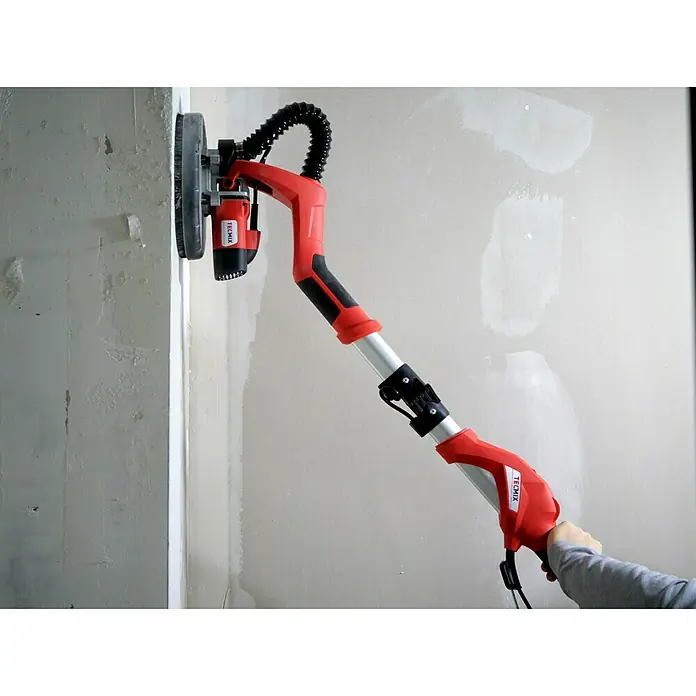 Berg Tecmix Wand- & Deckenschleifer TM LHS 710 D - 230 V, 710 W, Durchmesser Schleifteller: 225 mm - Ein roter Trockenbauschleifer der Marke Tecmix wird an einer unebenen Wand verwendet. Dieses Werkzeug erleichtert das Schleifen erheblich.
