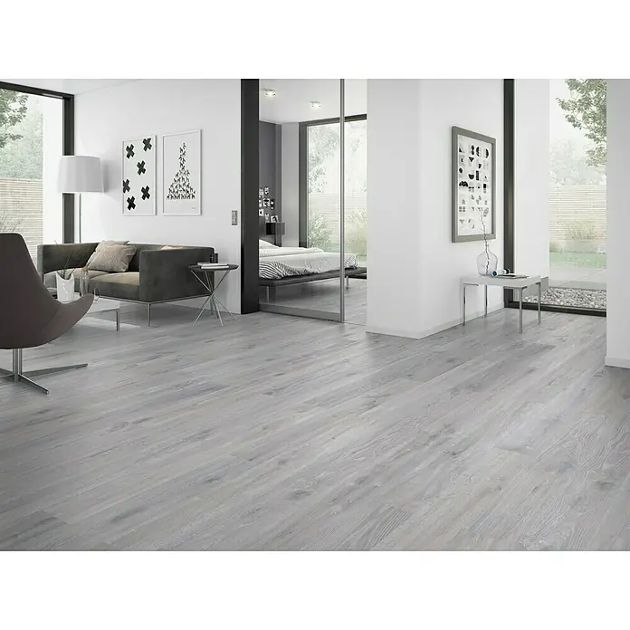 Classen Vinylbodenmuster GreenVinyl Eiche gekalkt Grau - 300 x 173 x 4 mm, Landhausdiele - Helles, modernes Wohnzimmer mit grauem Holzboden, grauer Couch und einem Schlafzimmer im Hintergrund, das durch eine Glasschiebetür abgetrennt ist.