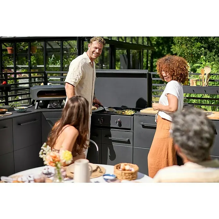 Cozze Plancha-Grill Combo 900 - Grillfläche (B x T): 79,3 x 46,3 cm, 7,5 kW, Anzahl Brenner: 3 Stk. - Eine stilvolle Außenküche mit Grill, Pizzaofen und Arbeitsflächen, umgeben von fröhlichen Menschen.