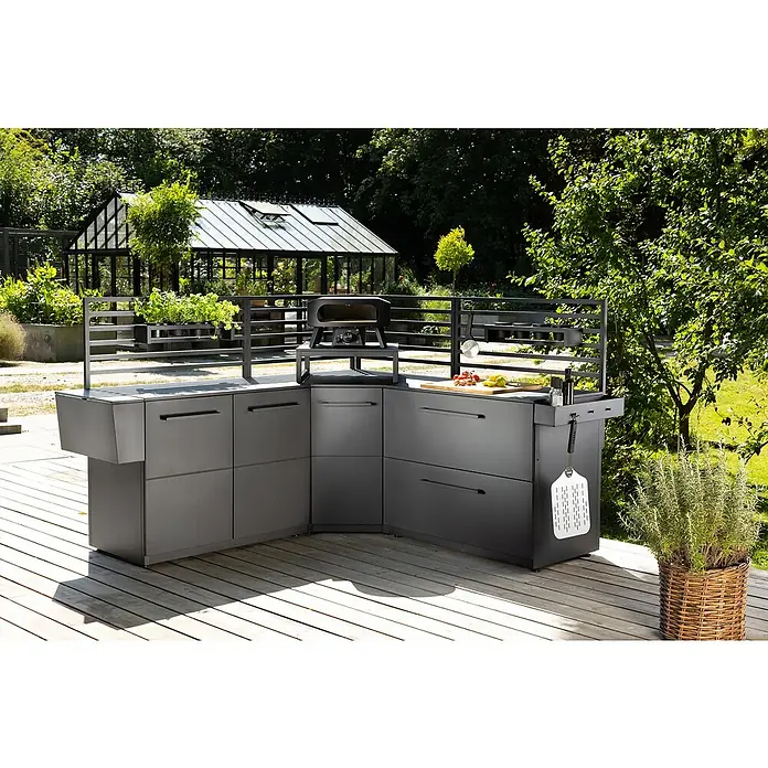 Cozze Elements Hängeregal - B x T x H: 60 x 13 x 10 cm, Schwarz, Passend für: Cozze Elements Outdoorküchen Module - Diese Aufnahme zeigt eine moderne Outdoor-Küche mit Grill, Arbeitsfläche und Stauraum auf einer Holzterrasse mit Gartengewächshaus im Hintergrund.