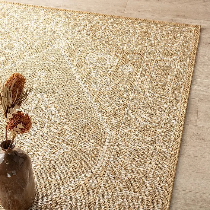Dekoria Flachgewebeteppich - karamellfarben, 230 x 160 cm - Nahaufnahme eines beigen Teppichs mit filigranem Muster und einer braunen Vase mit getrockneten Blumen auf einem Holzboden.