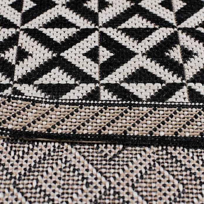 Dekoria Flachgewebeteppich - weiß, schwarz, 170 x 120 cm - Nahaufnahme eines dekorativen Kissens mit einem schwarz-weißen geometrischen Muster und einer verzierten Borte.