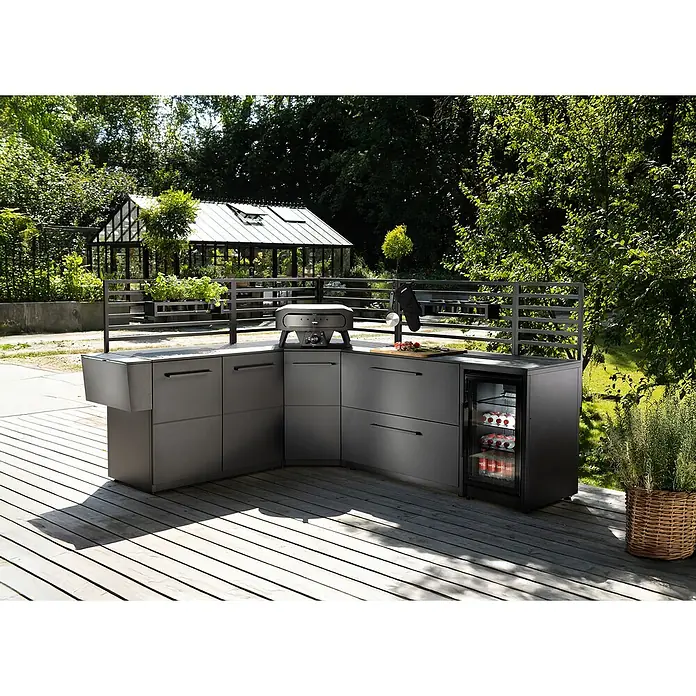 Cozze Elements Arbeitsplatte - HPL (Hochdrucklaminat), B x T x H: 49,5 x 60 x 1,5 cm - Graue Outdoor-Küche mit Grill, Kühlschrank und Spüle auf einer Holzterrasse mit Blick auf ein Gewächshaus. Ideal für kulinarische Erlebnisse im Freien.