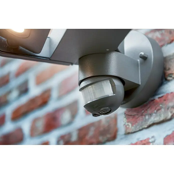 Lutec Aplique LED con sensor - 9 W, L x An x Al: 23 x 23 x 13,5 cm, Gris, Blanco neutro - Primer plano de un sensor de movimiento montado en una pared de ladrillos, que proporciona seguridad exterior mejorada.