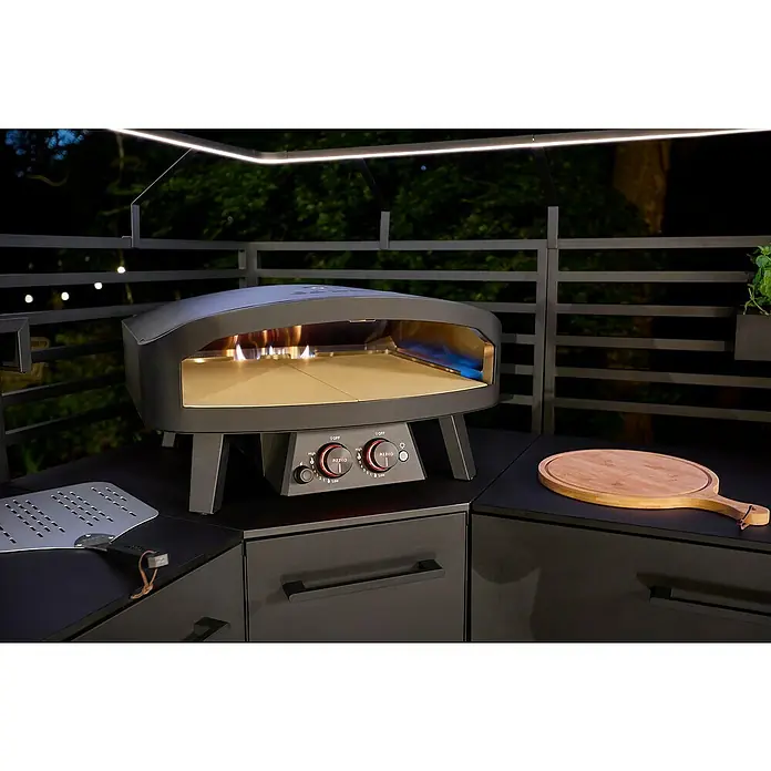 Cozze Pizzaofen Black Edition - Grillfläche (B x T): 60 x 60 cm - Nahaufnahme eines modernen Pizzaofens im Freien mit Bedienelementen, Pizzaschieber und Schneidebrett auf einer stilvollen schwarzen Arbeitsplatte.