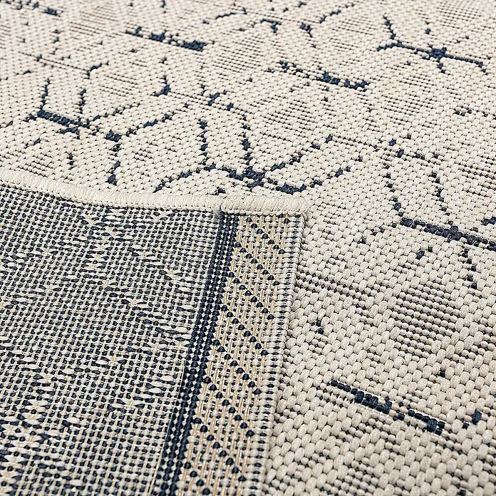 Dekoria Flachgewebeteppich - dunkelblau, creme, 230 x 160 cm - Nahaufnahme eines beigen Teppichs mit blauem Muster, der eine gewebte Textur und Details zeigt.\n