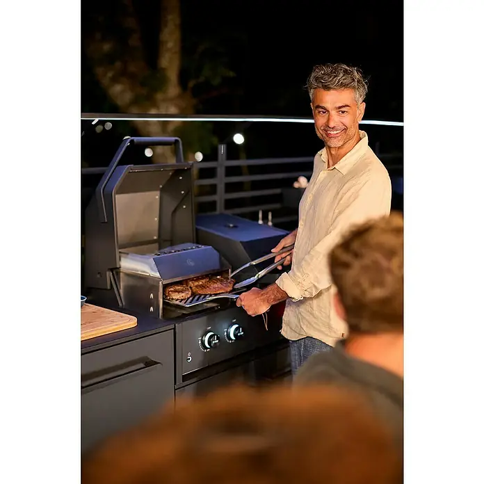 Cozze Hybrid-Grill Quattro 900 - Grillfläche (B x T): 72,7 x 34,5 cm, 13 kW, Anzahl Brenner: 3 Stk. - Mann grillt Steaks auf einem modernen Grill mit LED-Beleuchtung. Der Grill verfügt über Knöpfe und ist stilvoll designt.