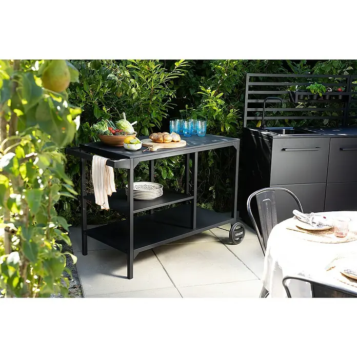 Cozze Elements Beistelltisch - Schwarz, B x T x H: 115 x 60 x 90 cm - Ein schwarzer Servierwagen mit frischen Zutaten, Gläsern und Geschirr steht im Garten, ergänzt durch eine Außenküche.