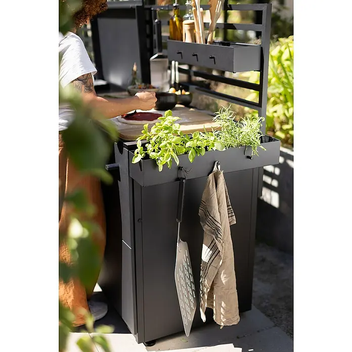 Cozze Elements Hängeregal - B x T x H: 60 x 13 x 10 cm, Schwarz, Passend für: Cozze Elements Outdoorküchen Module - Schwarze Outdoor-Küche mit Kräutern, Utensilien und Handtuch, während eine Person Pizza zubereitet. Ideal zum Kochen im Freien.