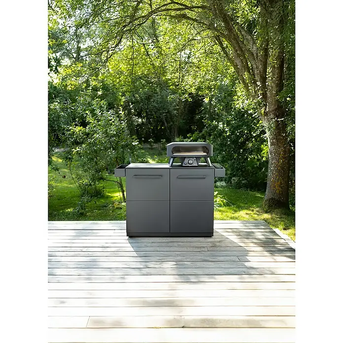 Cozze Elements Arbeitsplatte - HPL (Hochdrucklaminat), B x T x H: 110 x 60 x 1,5 cm - Ein grauer Outdoor-Küchenschrank mit einem Pizzaofen auf einer Holzterrasse im Grünen. Der Küchenschrank bietet Stauraum und Arbeitsfläche.