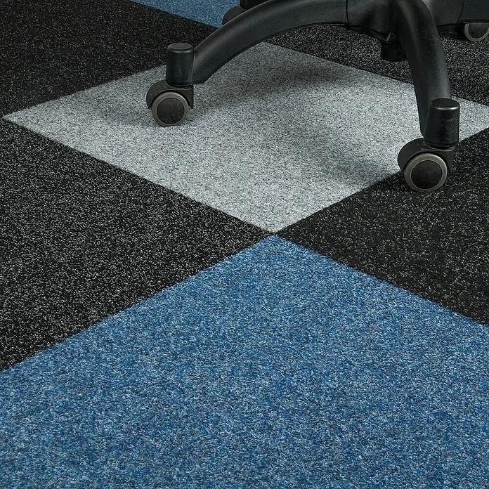 Bricoflor Teppichfliese - Breite: 50 cm, Nadelfilz, Polypropylen, grau - Nahaufnahme von Teppichfliesen in Schwarz, Grau und Blau, die ein geometrisches Muster bilden. Ein Bürostuhl ist teilweise im Bild zu sehen.