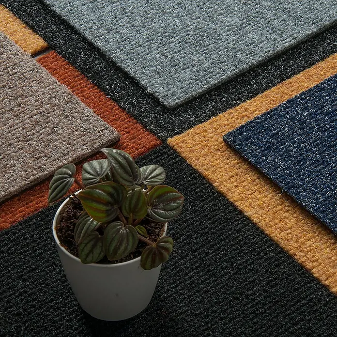 Bricoflor Teppichfliese - Breite: 50 cm, Nadelfilz, Polypropylen, schwarz - Ein quadratisches Arrangement verschiedenfarbiger Teppichfliesen, ergänzt durch eine Topfpflanze, die Textur und Farbe in den Vordergrund stellt.