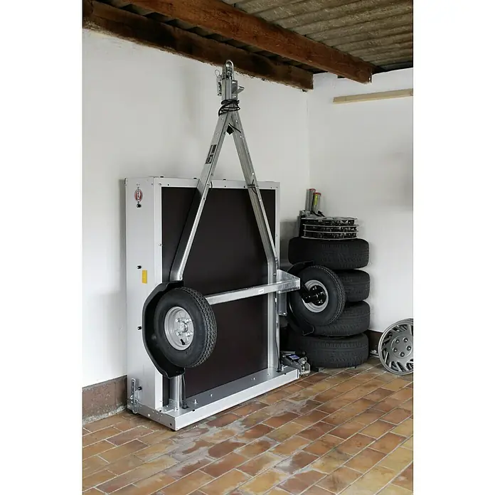 Stema Anhänger Mini 350 - Nutzlast: 270 kg, Einachser, 134x 108 x 26,5 cm, Ungebremst - Das Bild zeigt einen hochgeklappten Anhänger mit silbernem Rahmen und schwarzen Seitenwänden in einer Garage, um Platz zu sparen.