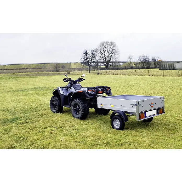 Stema Anhänger Mini 350 - Nutzlast: 270 kg, Einachser, 134x 108 x 26,5 cm, Ungebremst - Das Bild zeigt einen Can-Am Geländewagen mit Anhänger auf einem Feld, ideal für den Transport von Lasten im Gelände oder auf der Straße.