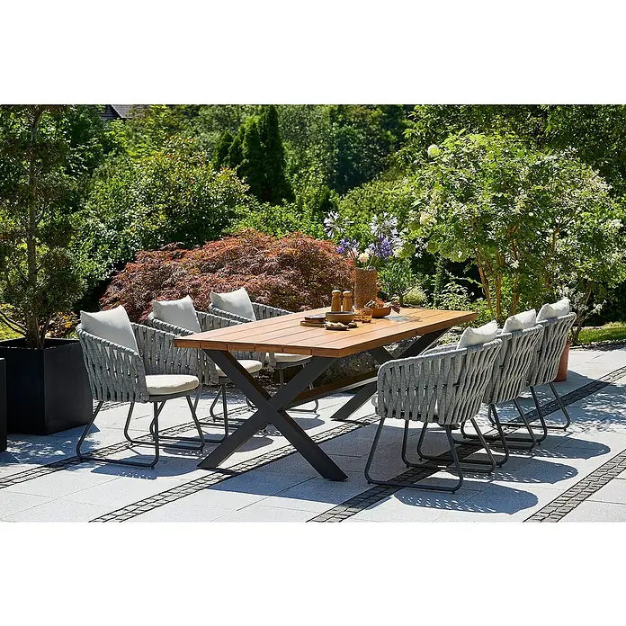 Sunfun Gartenmöbel-Set Maja Rope - 7 -tlg., Aluminium, Stahl, Eschenholz, Textilen, Anthrazit, Braun, Grau-Beige - Ein einladender Außenbereich mit einem Esstisch aus Holz und grauen Stühlen mit hellen Kissen, umgeben von üppigem Grün.