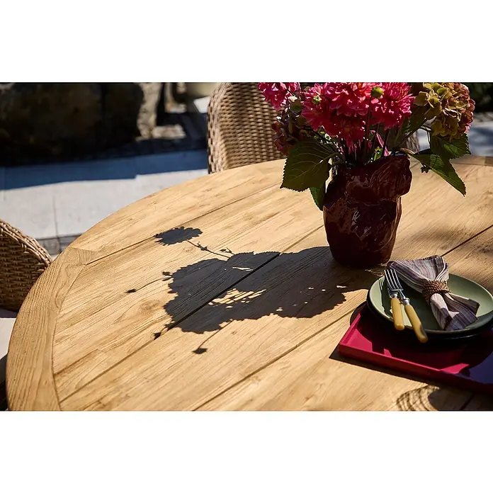 Gartentisch rund - Ø x H: 150 x 65 cm, Teak, Aluminium, Braun/Anthrazit, Low-Dining - Ein runder Holztisch im Freien mit Blumen in einer Vase und einem Gedeck auf einer roten Unterlage, ideal für Mahlzeiten im Garten.